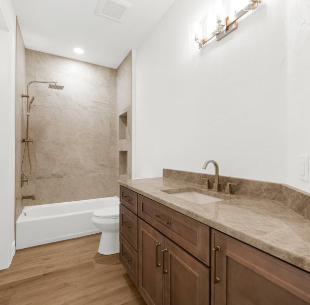 Bathroom with beige tile shower, brown vanity, wood flooring.