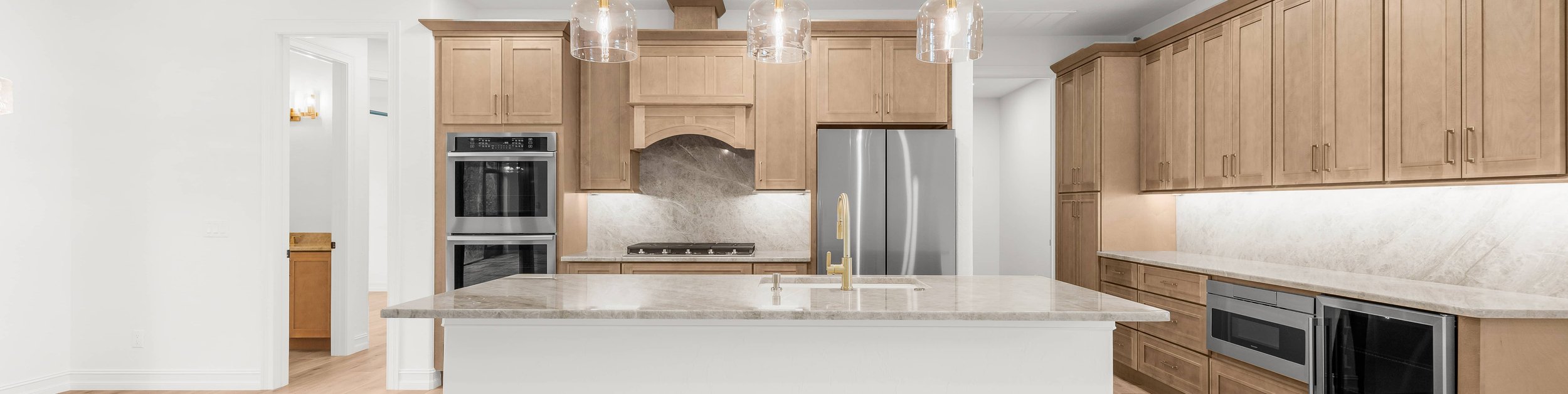 Kitchen with wood cabinets, white island, glass pendant lights.