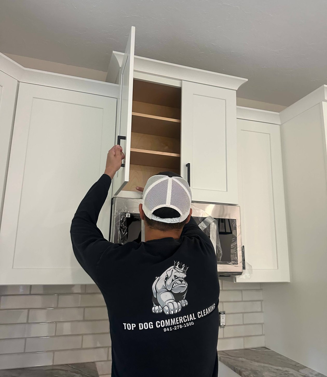 Cleaner reaching into white cabinet above stove in kitchen.