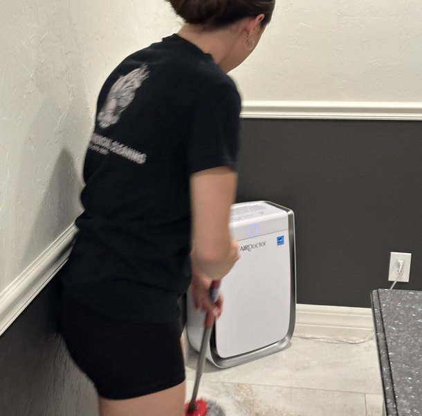 Woman vacuuming hallway with air purifier beside her.