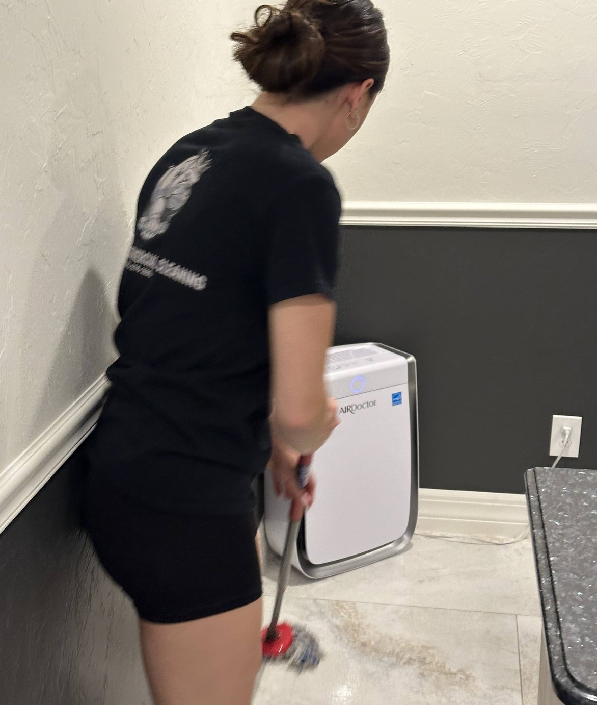 Woman vacuuming hallway with air purifier beside her.