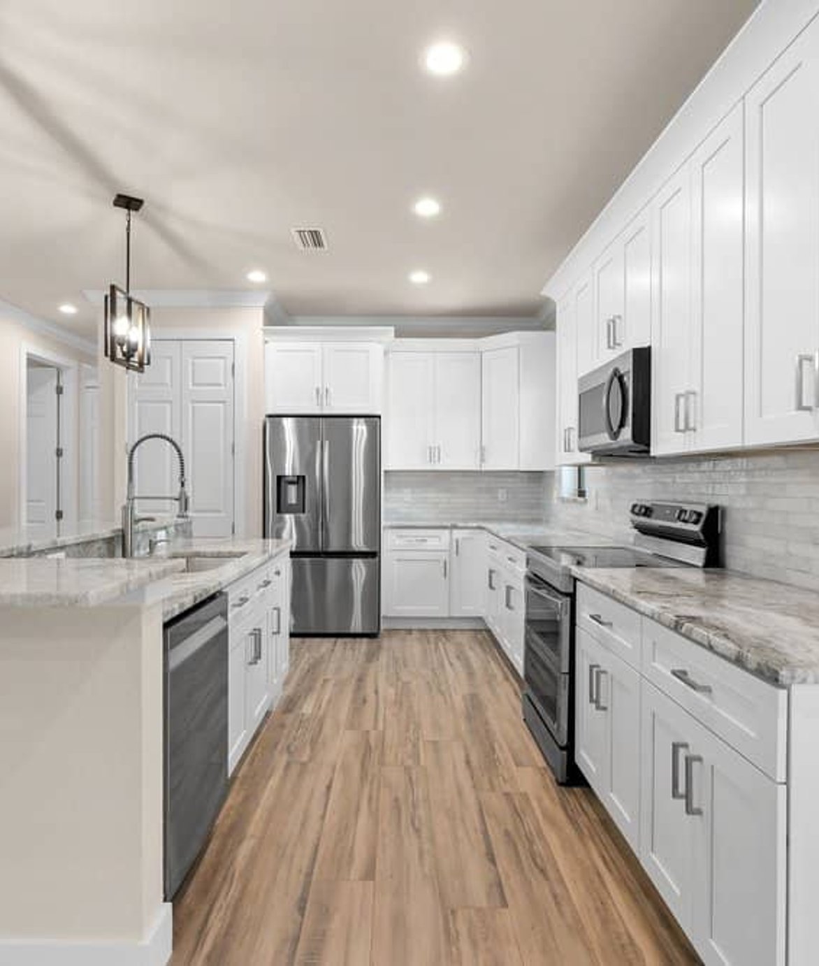 White kitchen with island, stainless appliances, wood-look flooring.